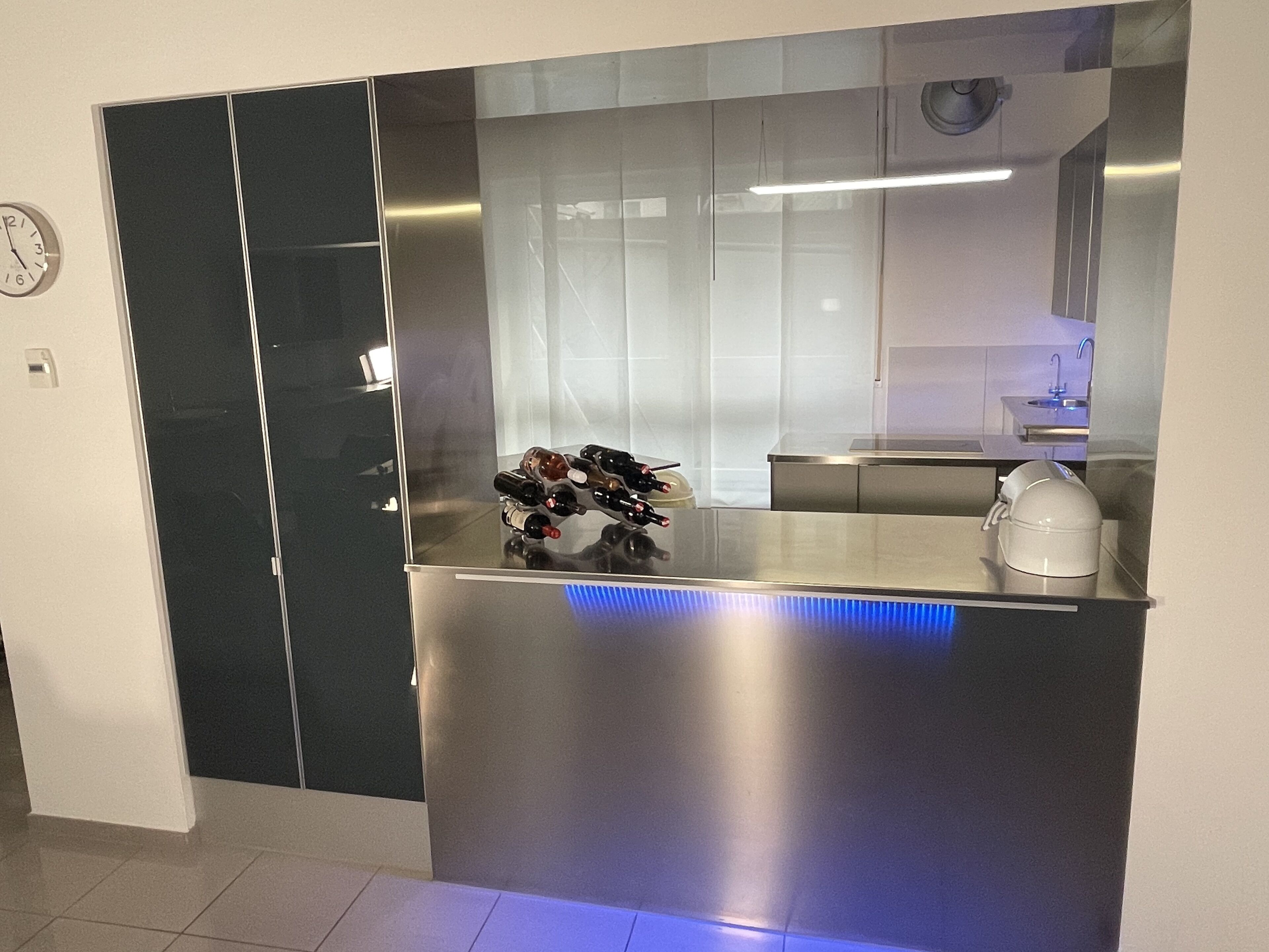 A modern kitchen with a stainless steel countertop, a wine rack, and a clock on the wall.