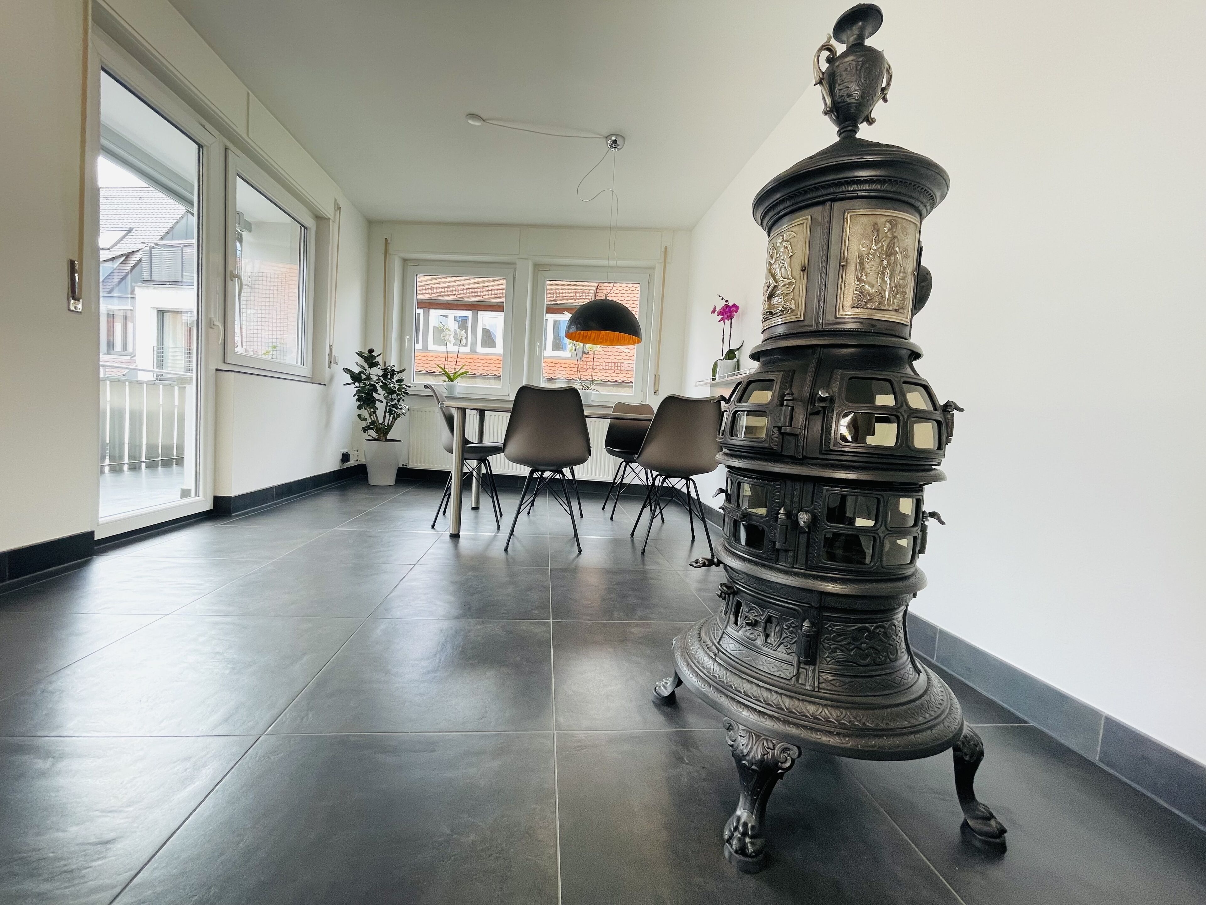 Amplia habitación con un gran ventanal, una mesa de comedor con sillas y una estufa de metal decorativa.