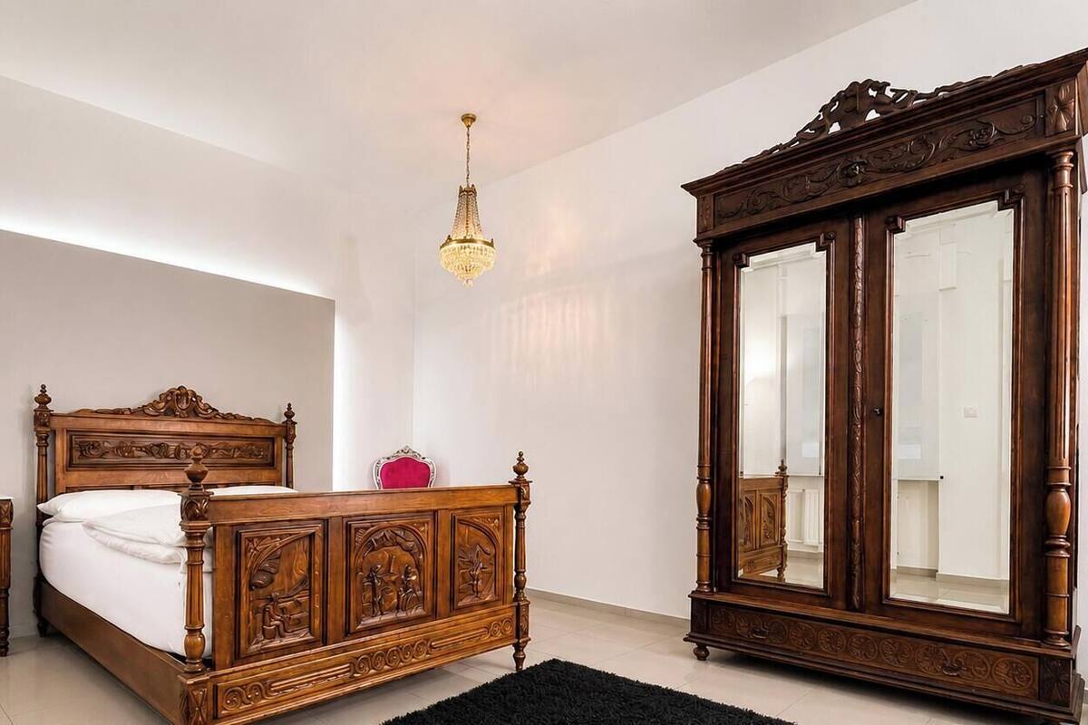 Un dormitorio con una cama de madera, una mesita de noche, un espejo grande y un candelabro.