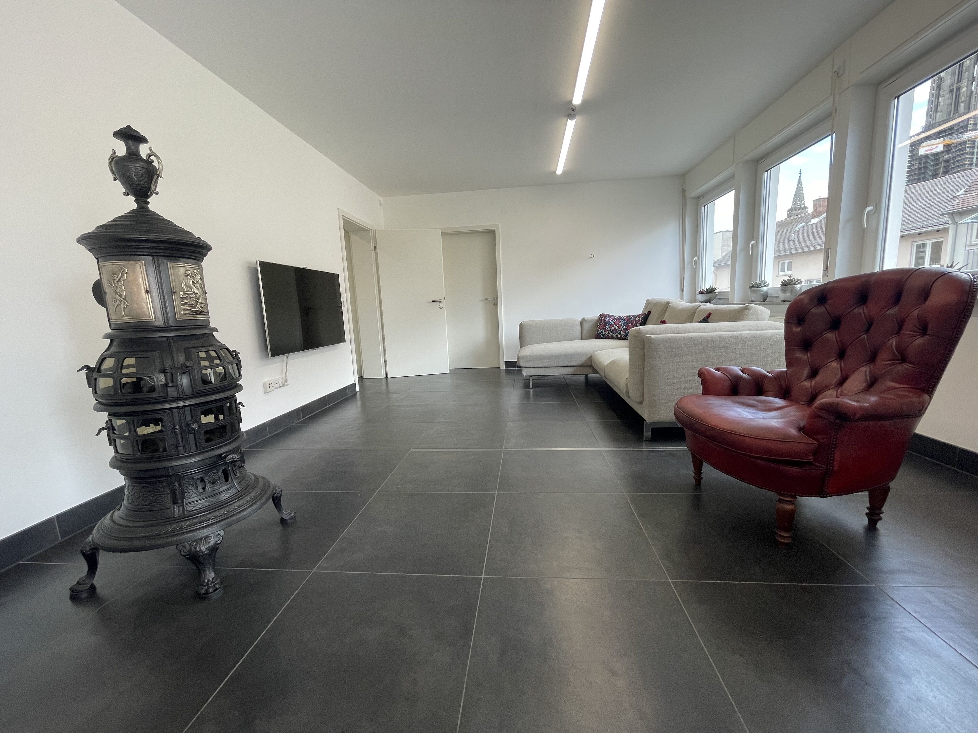 Un salón moderno con piso de baldosas oscuras, un sillón de cuero rojo, un sofá blanco y un jarro decorativo negro.