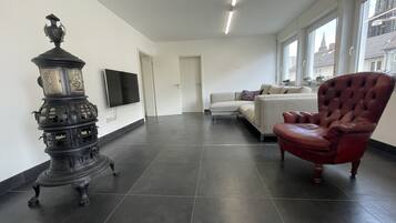 Un salón moderno con piso de baldosas oscuras, un sillón de cuero rojo, un sofá blanco y un jarro decorativo negro.