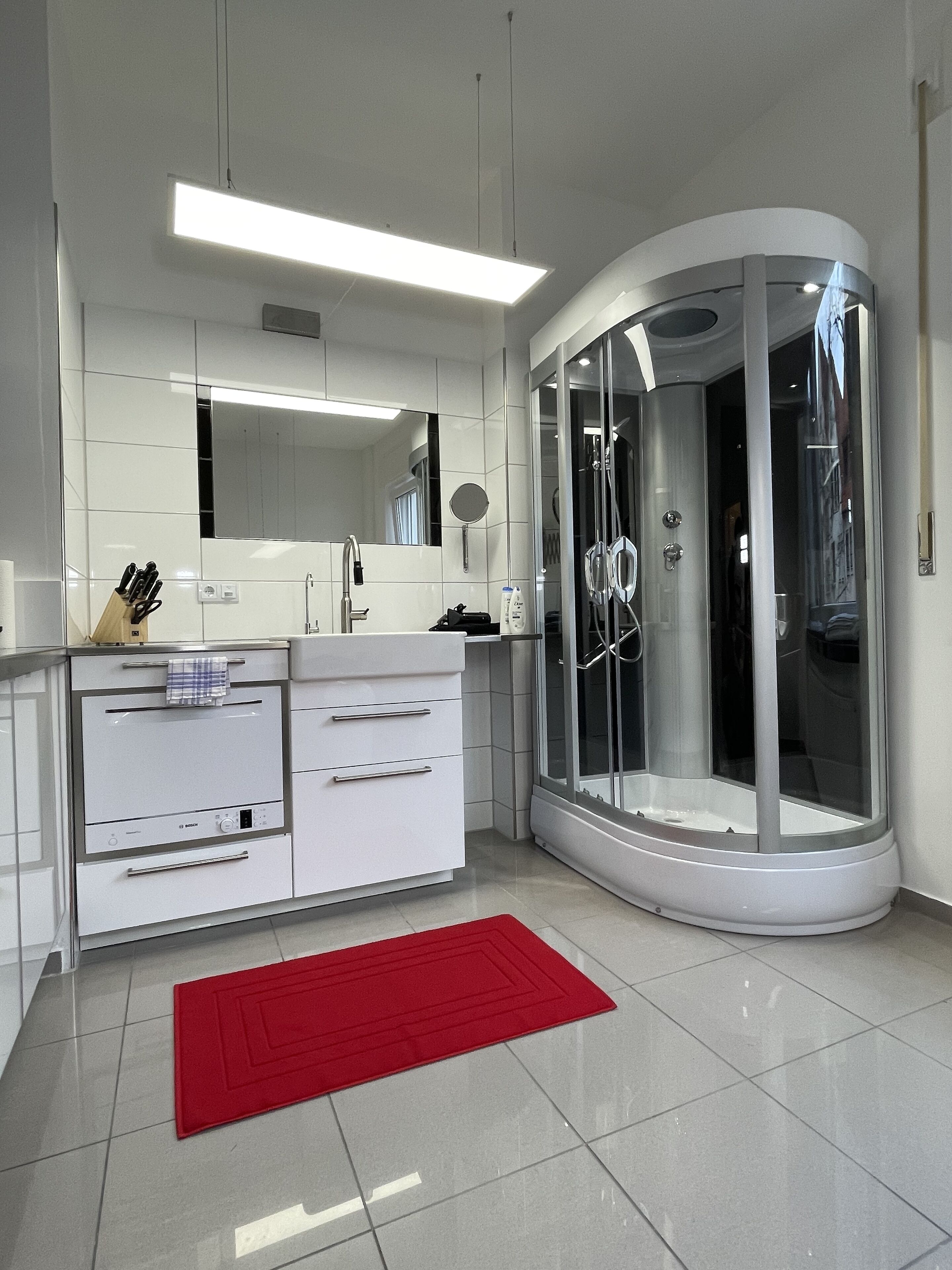 A modern bathroom with a glass-enclosed shower, a white vanity with a mirror, and a red rug on the floor.