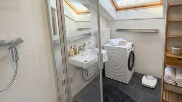 A modern bathroom with a skylight, a glass shower enclosure, a built-in sink, a washing machine, and a towel rack.