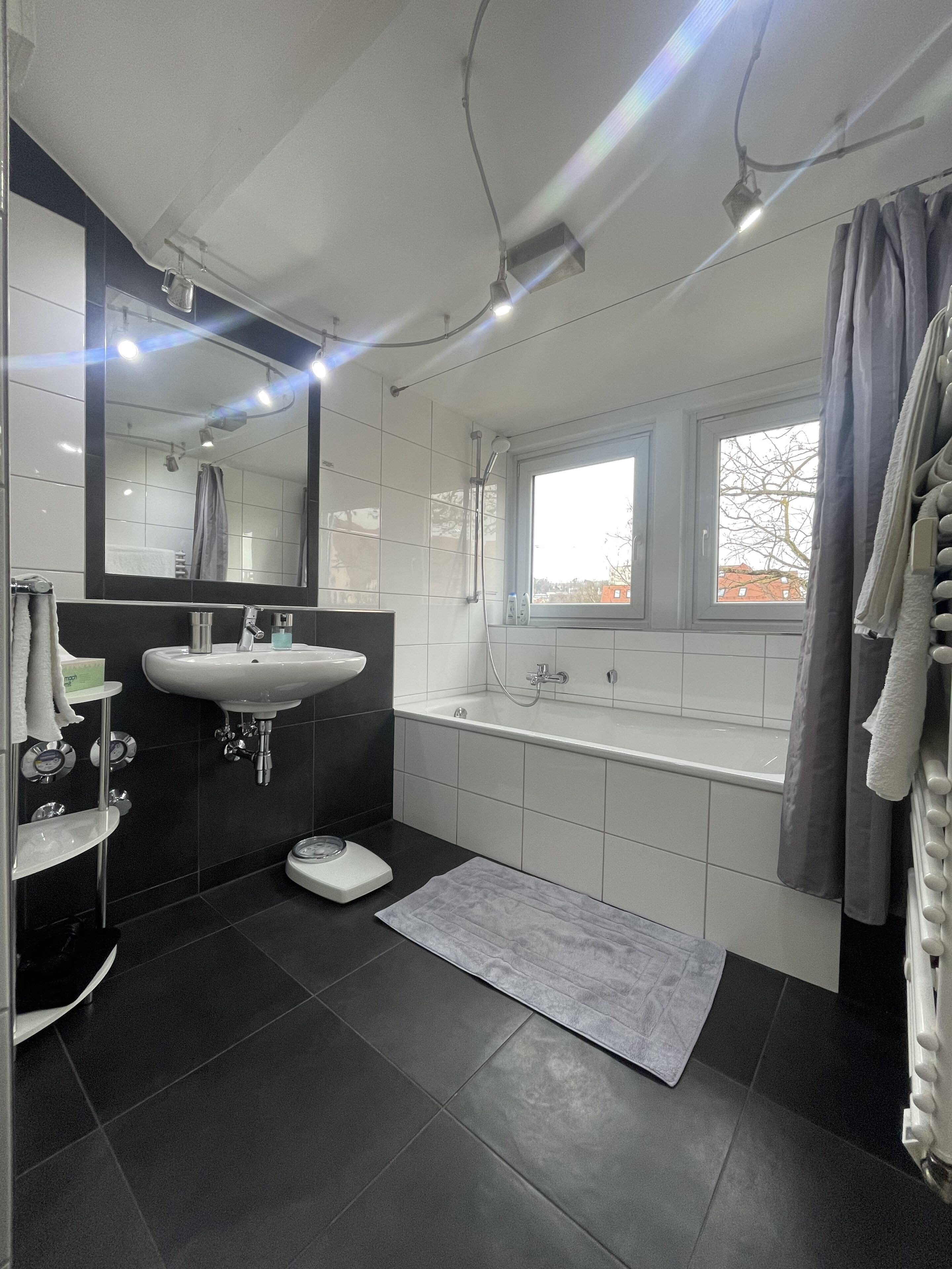 Ein modernes Badezimmer mit einem großen Spiegel, zwei Waschbecken, einer Badewanne und einem Fenster.