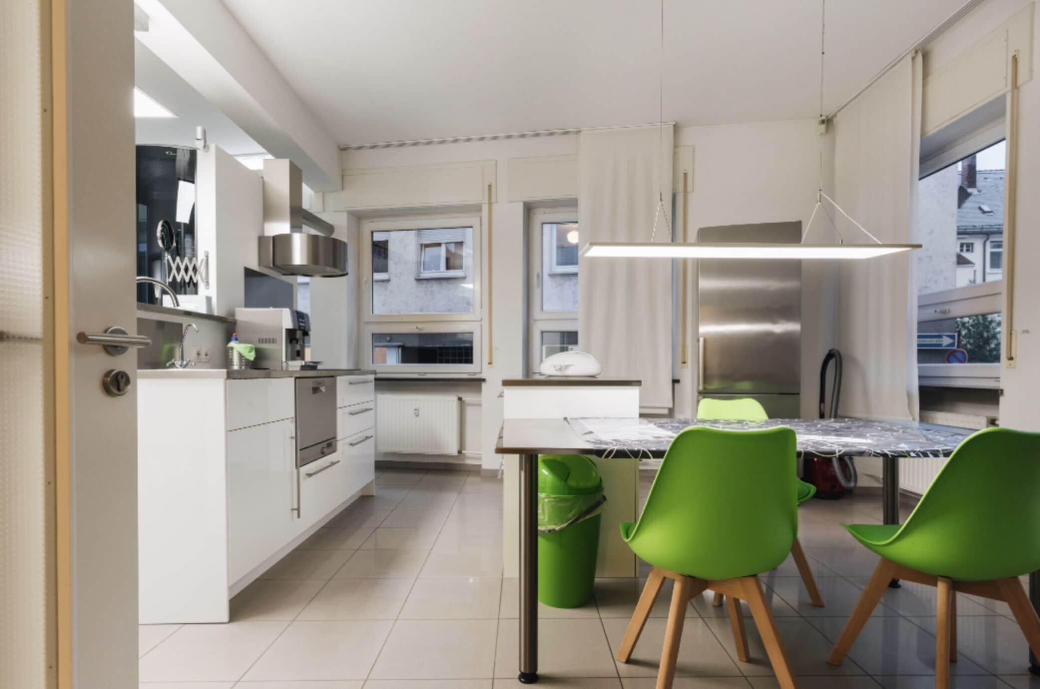 A modern kitchen with white cabinets, a stainless steel range hood, and a dining area with a table and green chairs.