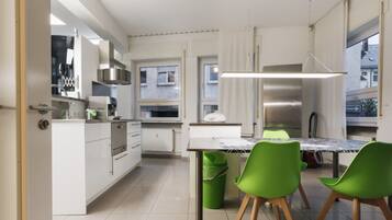 A modern kitchen with white cabinets, a stainless steel range hood, and a dining area with a table and green chairs.