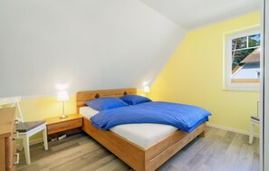 Un dormitorio con cama de madera, dos lámparas de noche, una mesita de noche, un escritorio y una ventana con vista a una casa.