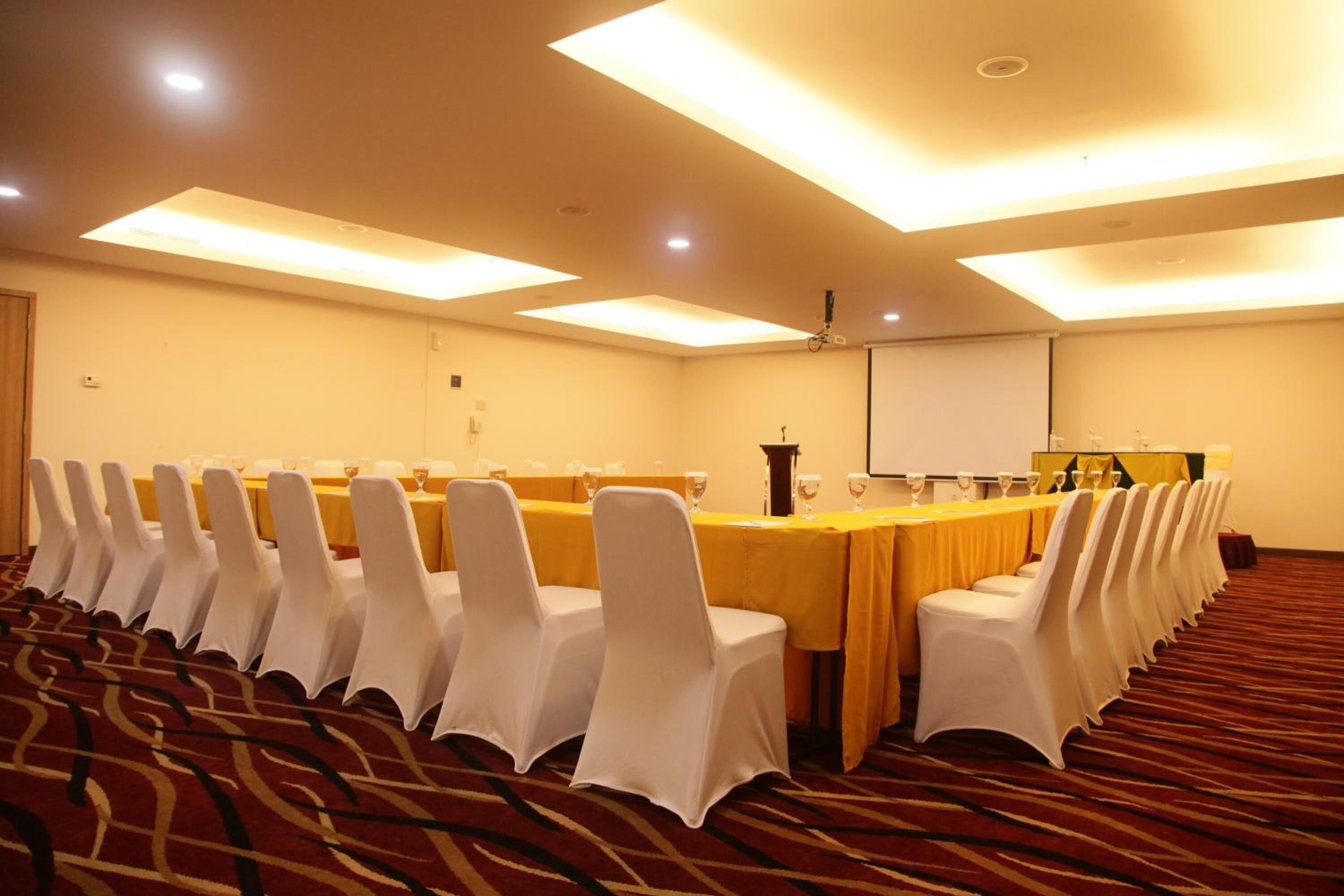 A conference room with a long table, white chairs, and a projector screen.