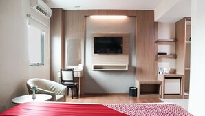 A modern hotel room with a bed, a chair, a small table, a TV mounted on the wall, and a trash bin. - Winstar Hotel (Pekanbaru)