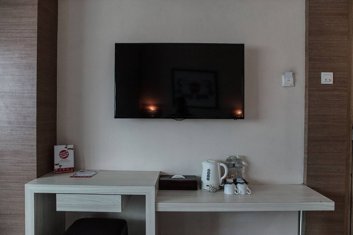 Une chambre d’hôtel équipée d’un téléviseur à écran plat fixé au mur, d’un bureau blanc avec une machine à café et d’une boîte de mouchoirs.