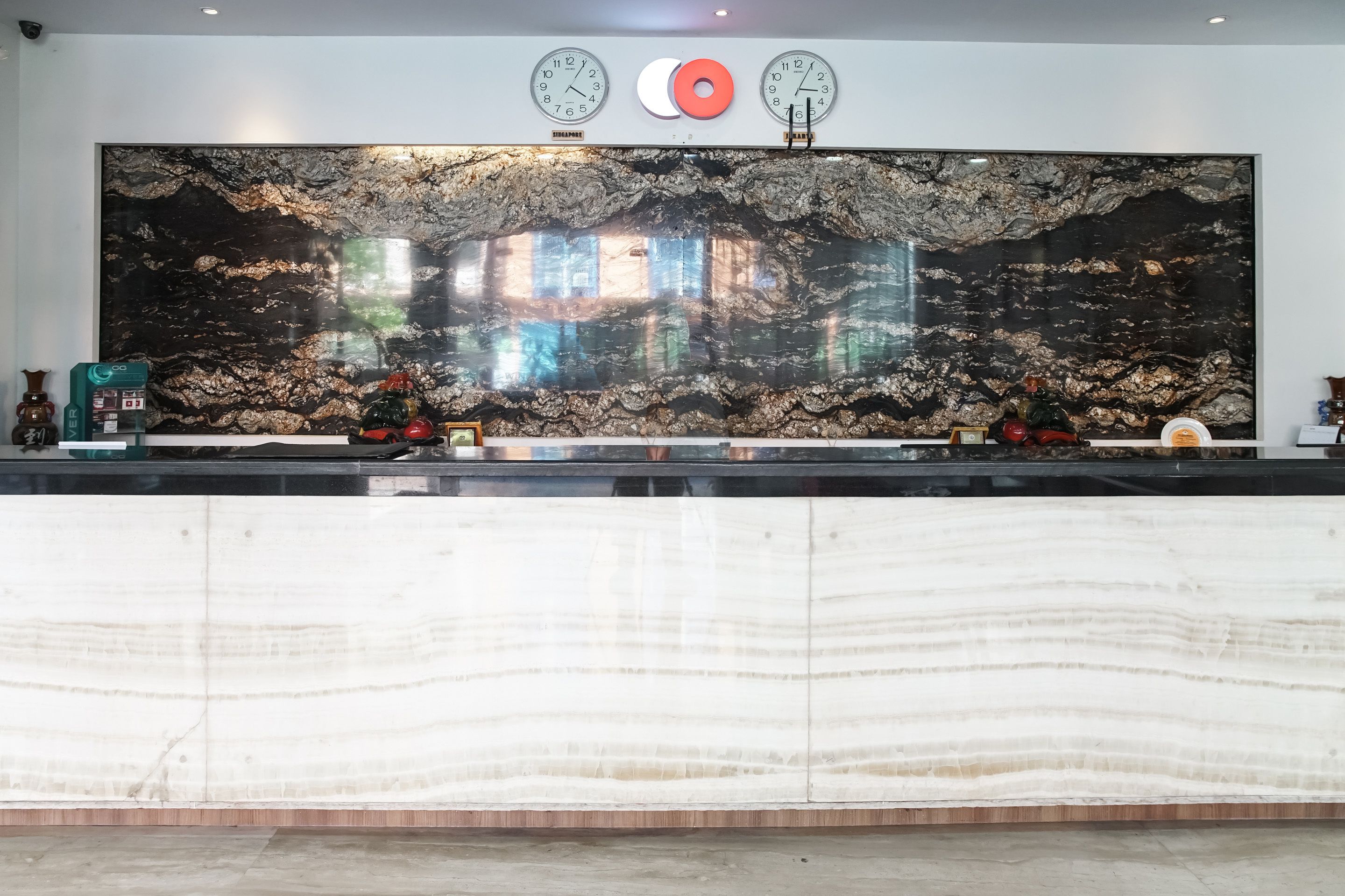 A reception area with a large marble counter, two wall clocks, and a decorative wall with a natural pattern.