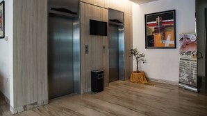 A modern elevator area with a wooden finish, a digital display, and a small trash bin. - Winstar Hotel (Pekanbaru)