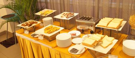 Una mesa de buffet con diferentes alimentos, como sándwiches, pasteles y un tostador.