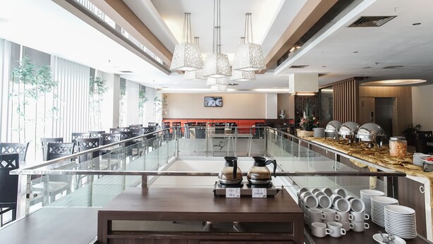 A modern hotel lobby with a glass railing, a buffet area with tea and coffee dispensers, and a television screen on the wall. - Winstar Hotel (Pekanbaru)