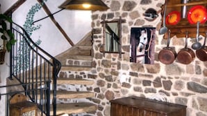Un intérieur rustique avec un mur en pierre, une malle en bois, un porte-ustensiles suspendu et un escalier.