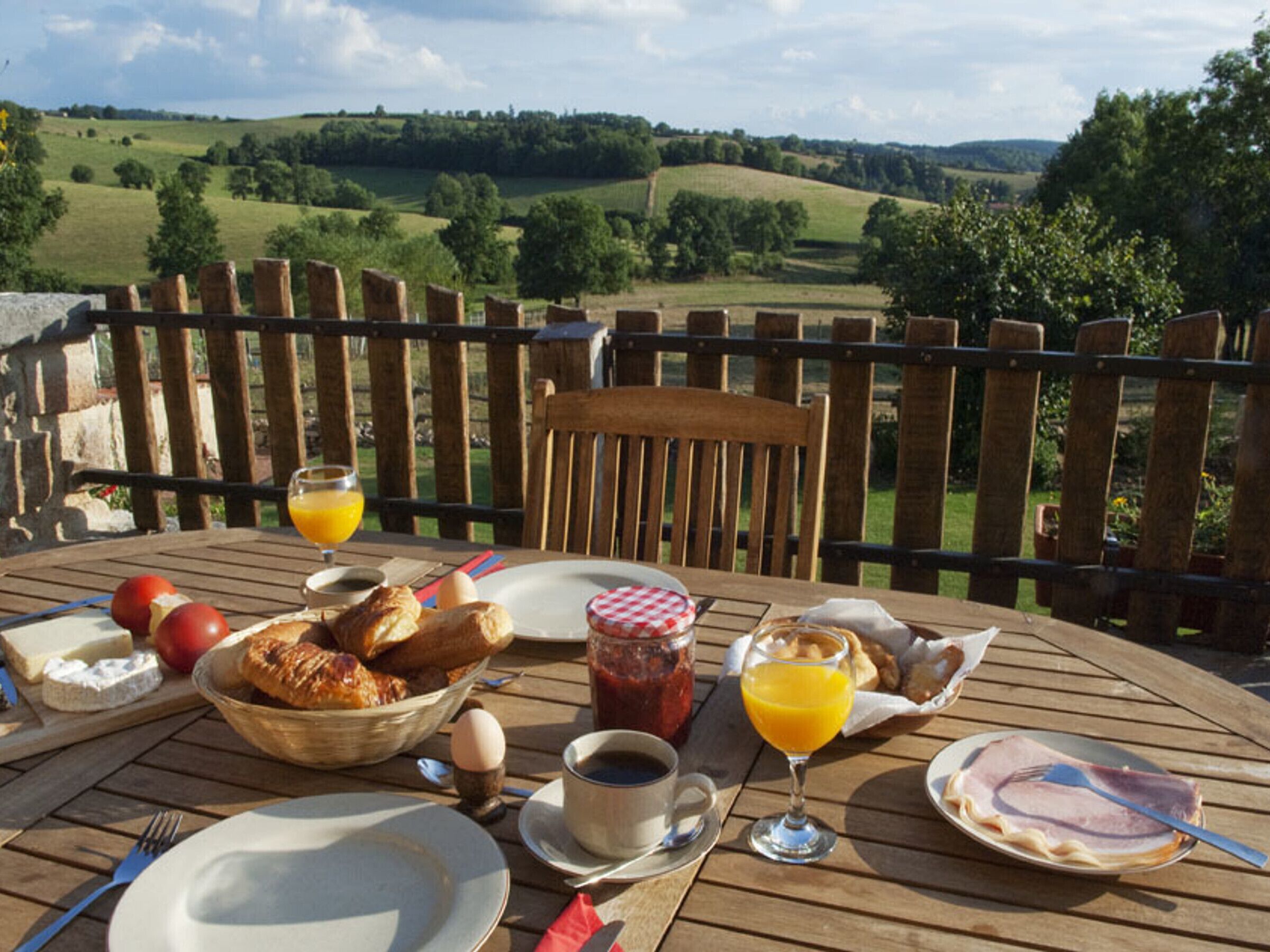 Ein mit Gebäck, Eiern und Orangensaft gedeckter Holztisch mit Blick auf eine malerische Landschaft.
