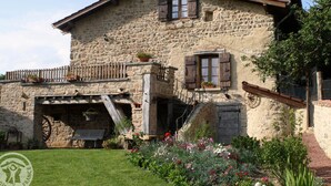 Un bâtiment en pierre doté d’un balcon en bois, d’une roue à eau et d’un jardin fleuri.