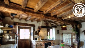 Une cuisine rustique avec des poutres apparentes, un sol en briques et un coin repas comprenant une table et des chaises.