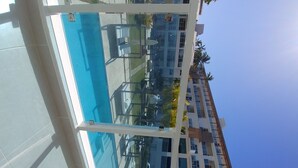 En moderne bygning med en glasfacade, et poolområde med liggestole og en klar blå himmel.