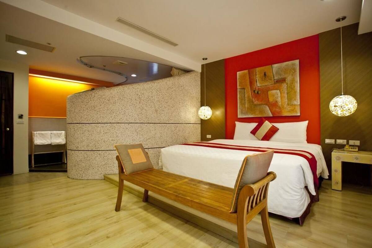 Una habitación de hotel moderna con una cama grande, un banco de madera, una mesita y una obra de arte colgada en la pared.