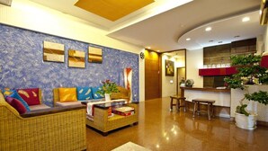 Un vestíbulo con mostrador de recepción, zona de estar con mobiliario de mimbre y una pared decorativa.