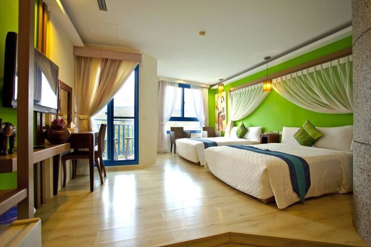 Habitación de hotel con dos camas, zona de comedor y vistas al exterior.