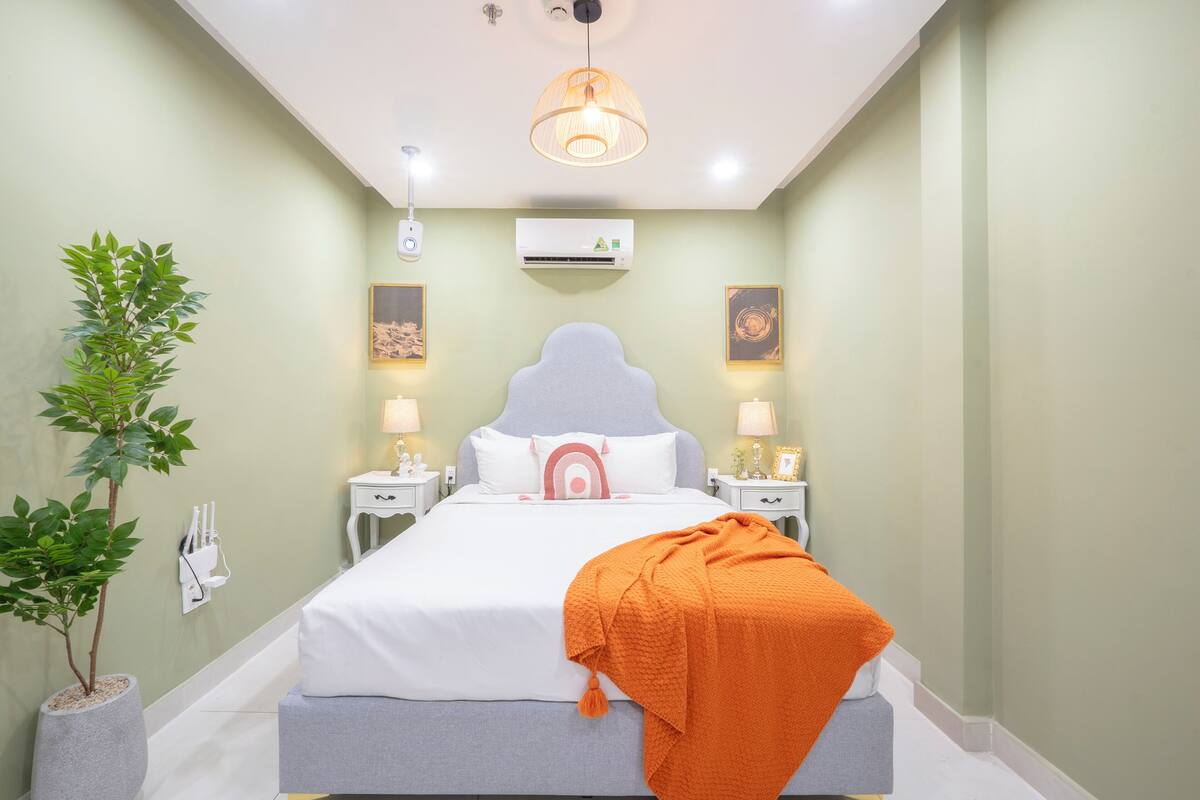 Een slaapkamer met een bed, nachtkastjes, een plant in pot en een airconditioning.