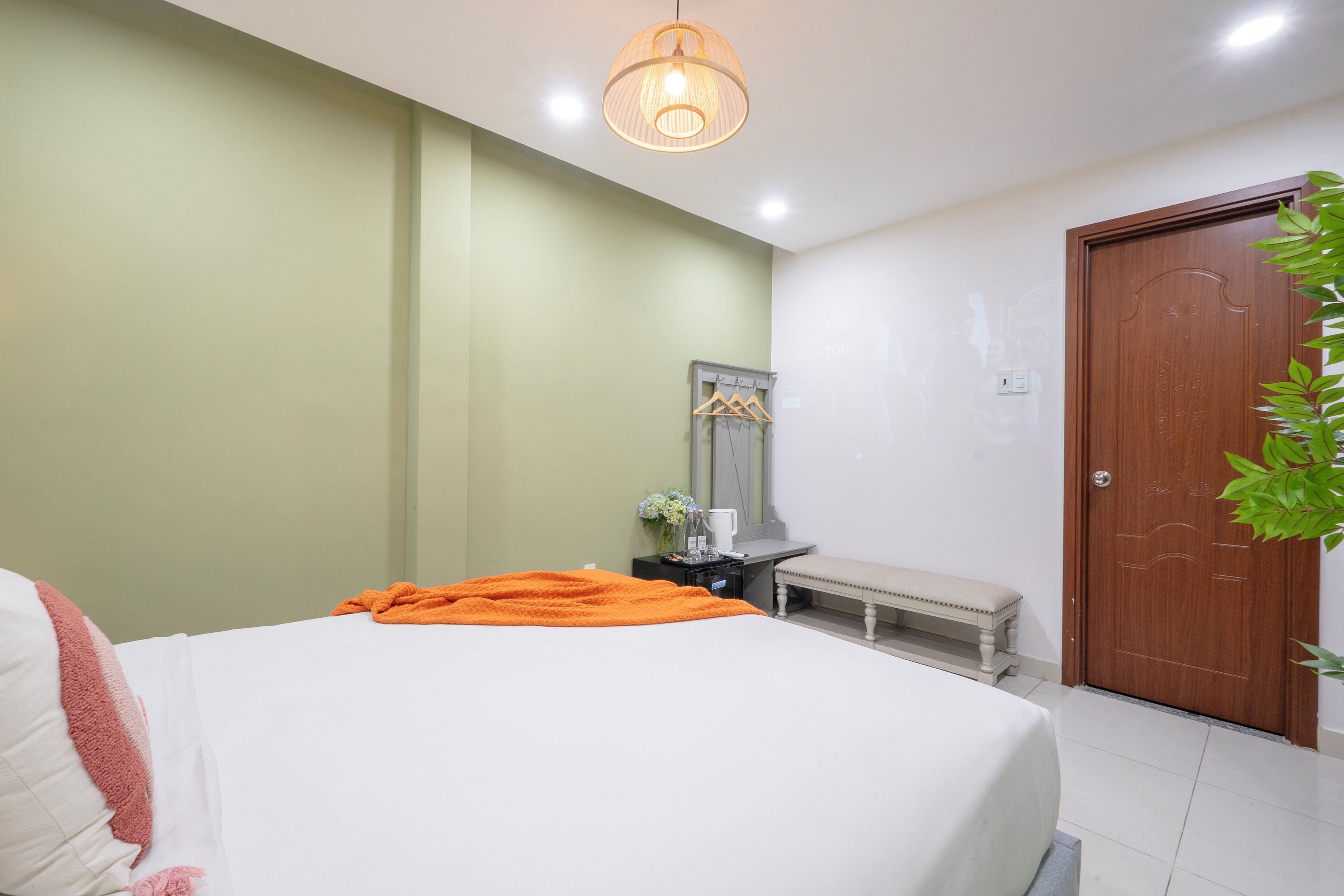A bedroom with a bed, a bench, a wooden door, and a hanging light fixture.