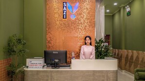 A reception desk with a sign reading "SAZI," a computer monitor, a check-in/out board, and a support phone number. - SAZI AMILA Nguyen Hue HOTEL - Free Banh Mi (Ho Chi Minh City)