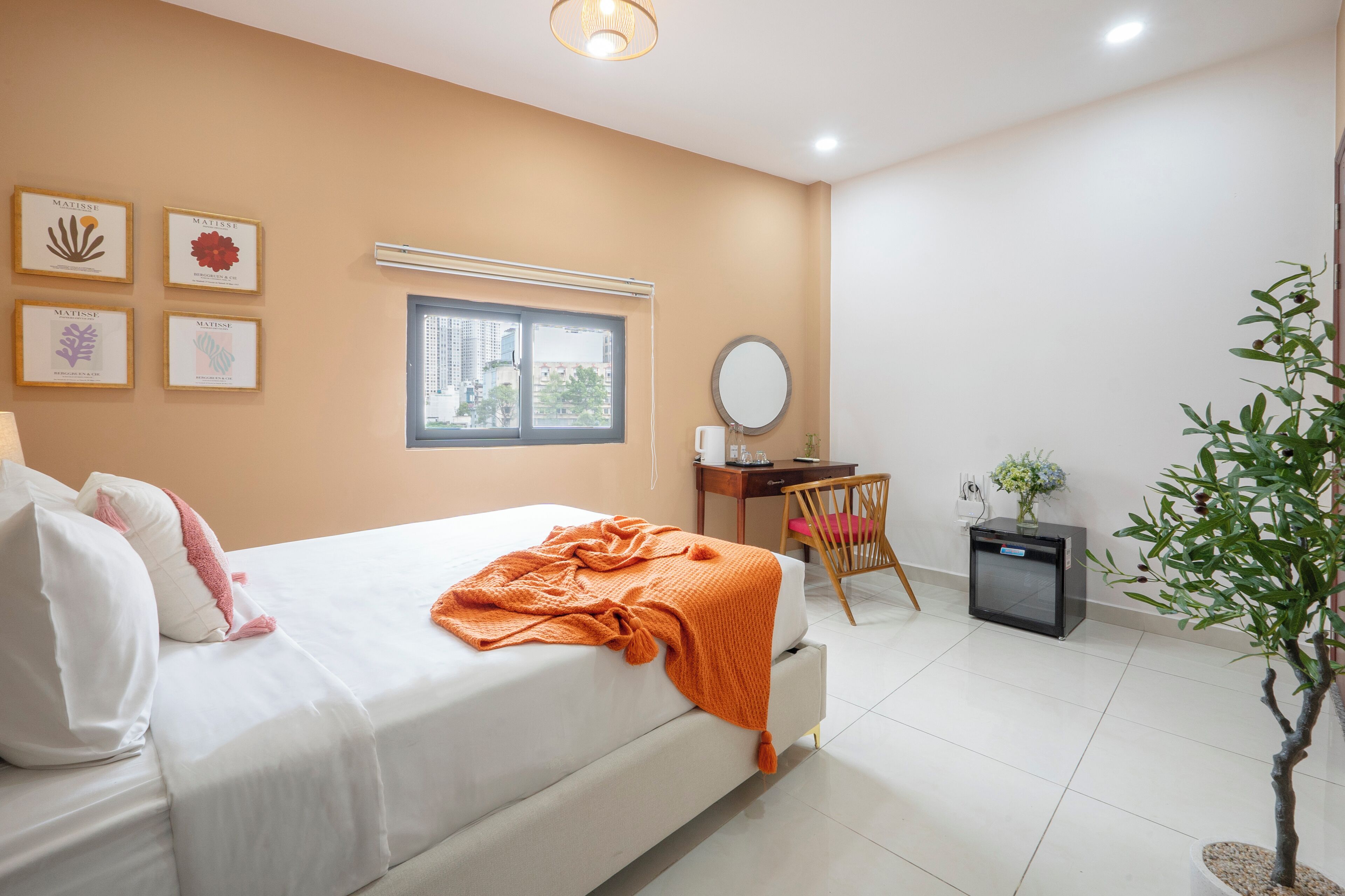 A bedroom with a bed, a desk, a chair, a small TV, and a potted plant.
