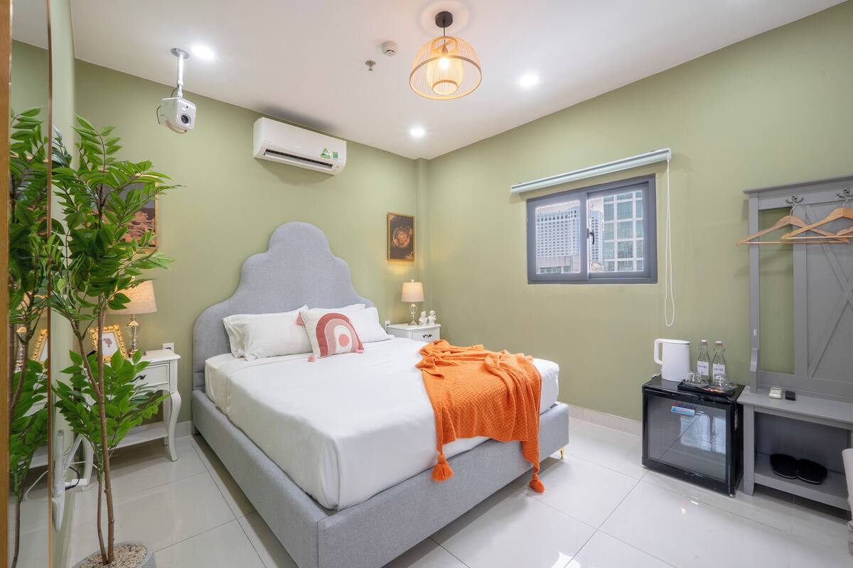 Een slaapkamer met een bed, nachtkastjes, een plant, een spiegel, een kledingkast en een raam.