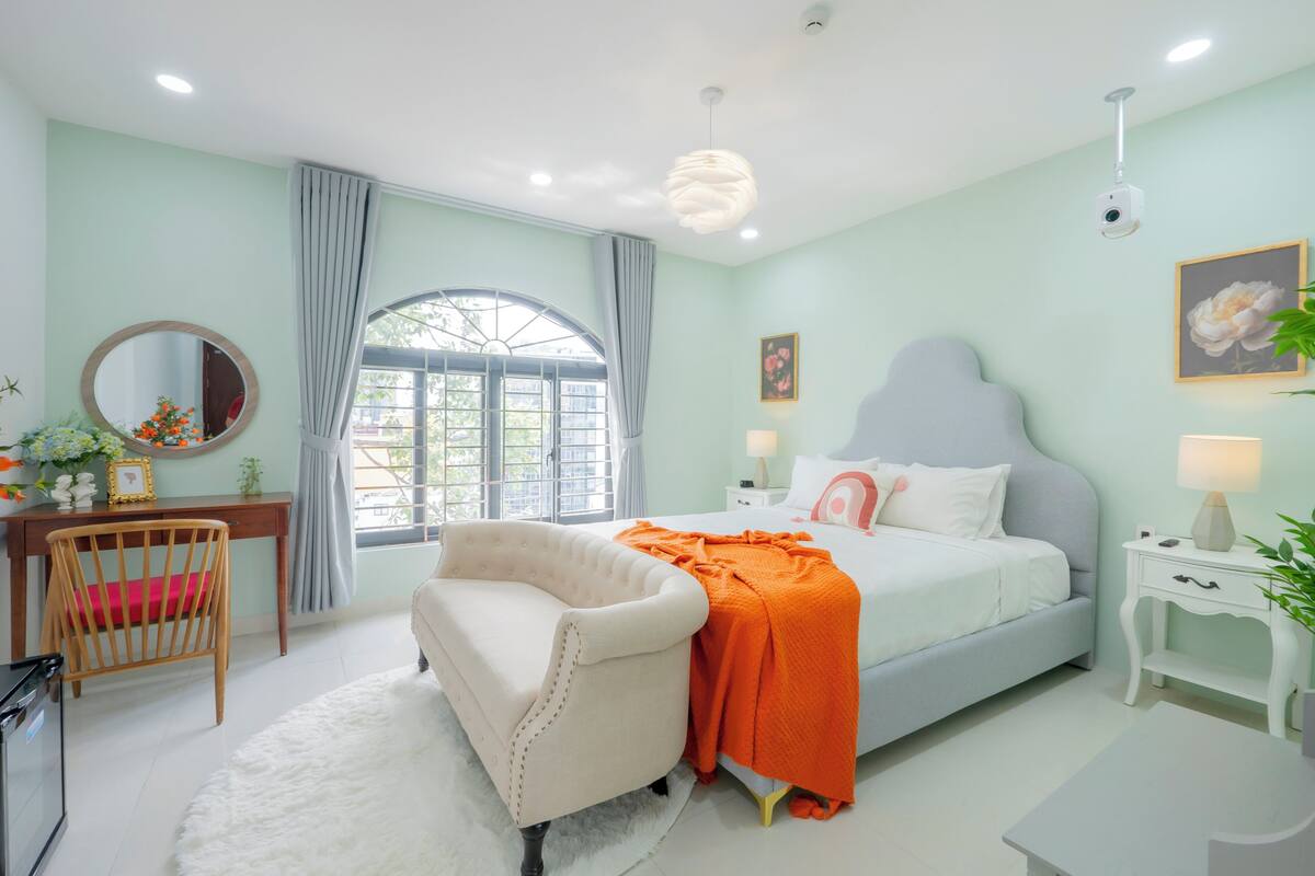 Een slaapkamer met een bed, een stoel, een bureau en een raam met gordijnen.