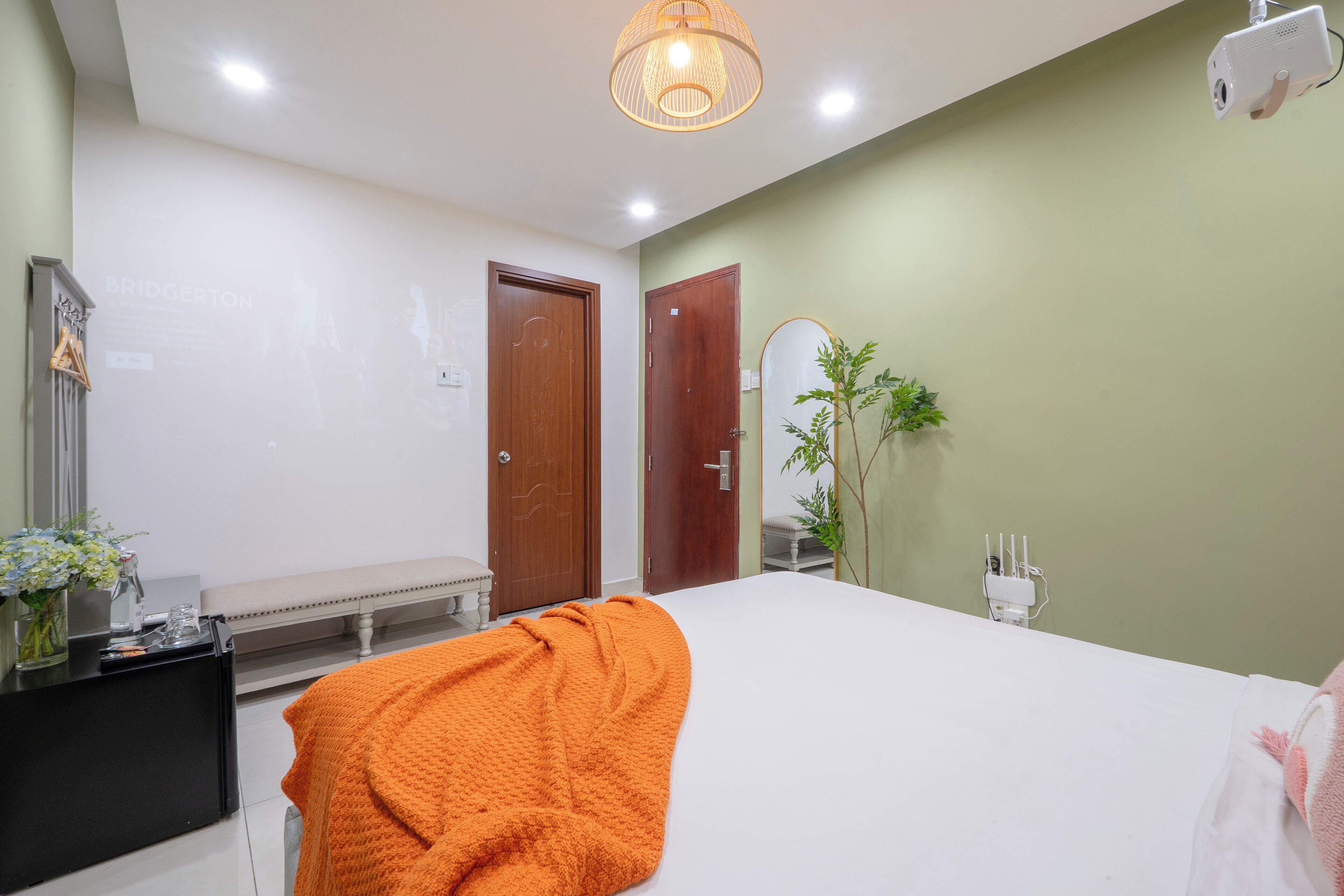 A hotel room with a bed, a desk, a mirror, and a plant.