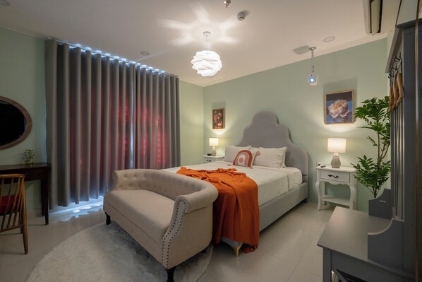 A modern bedroom with a bed, a chair, a nightstand, a lamp, and a plant.
