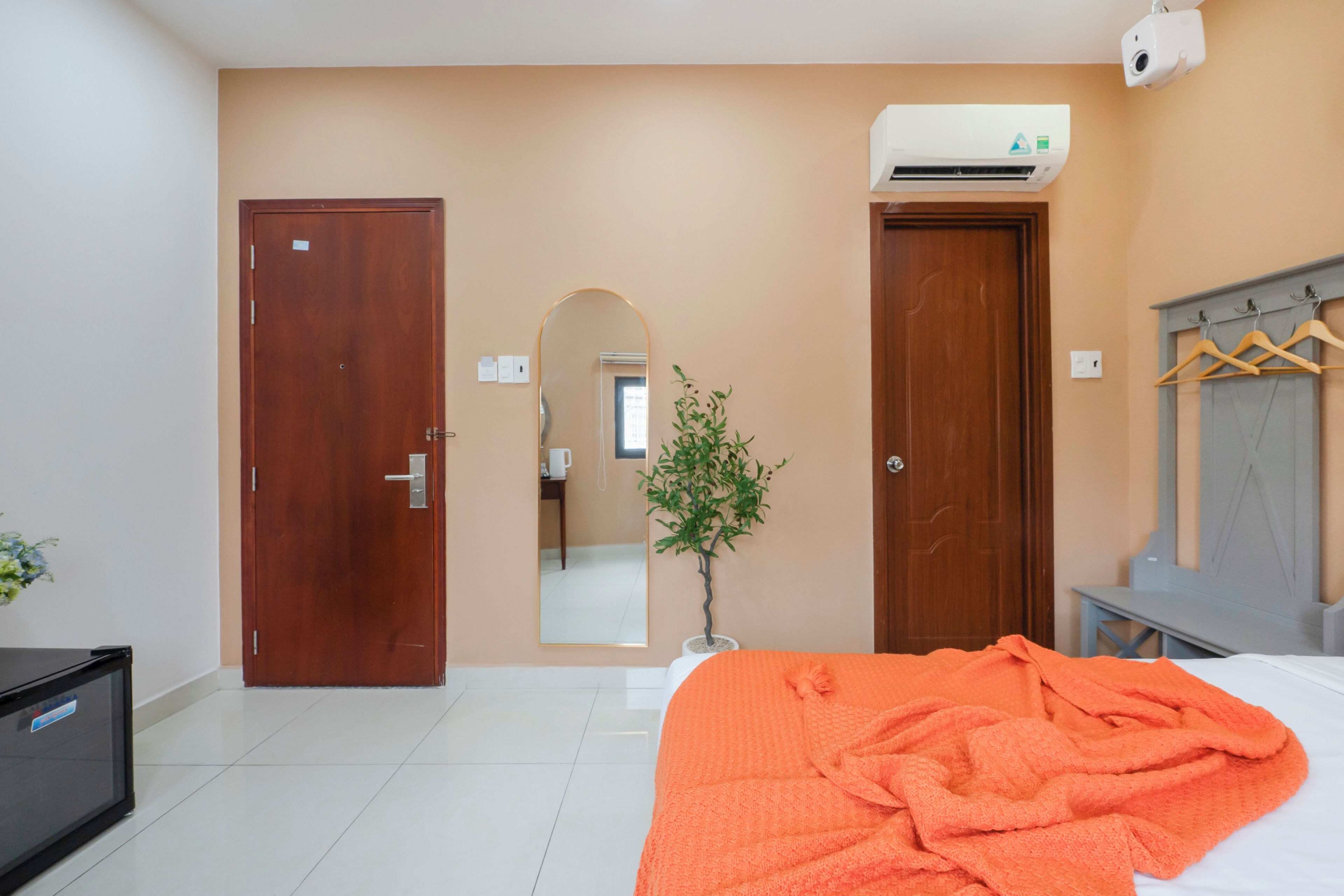 Quarto de hotel com cama, escrivaninha, espelho e porta.