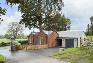 Une maison traditionnelle en briques, avec un garage, une clôture en bois et un grand arbre en arrière-plan.