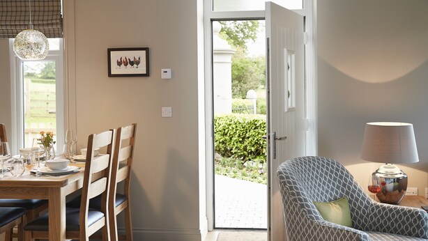 Un coin repas avec une table en bois dressée pour quatre personnes, un fauteuil à motifs et une porte donnant sur l’extérieur.