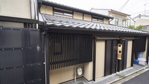 Une maison traditionnelle japonaise, avec un toit recouvert de tuiles, une porte coulissante et un petit hall d’entrée équipé d’une poubelle.