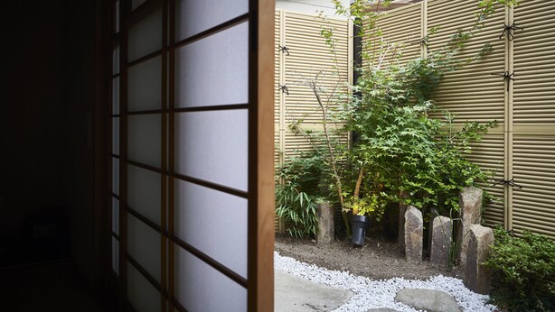 Un jardin japonais traditionnel, avec une clôture en bambou, des plantes en pot et un chemin de gravier.