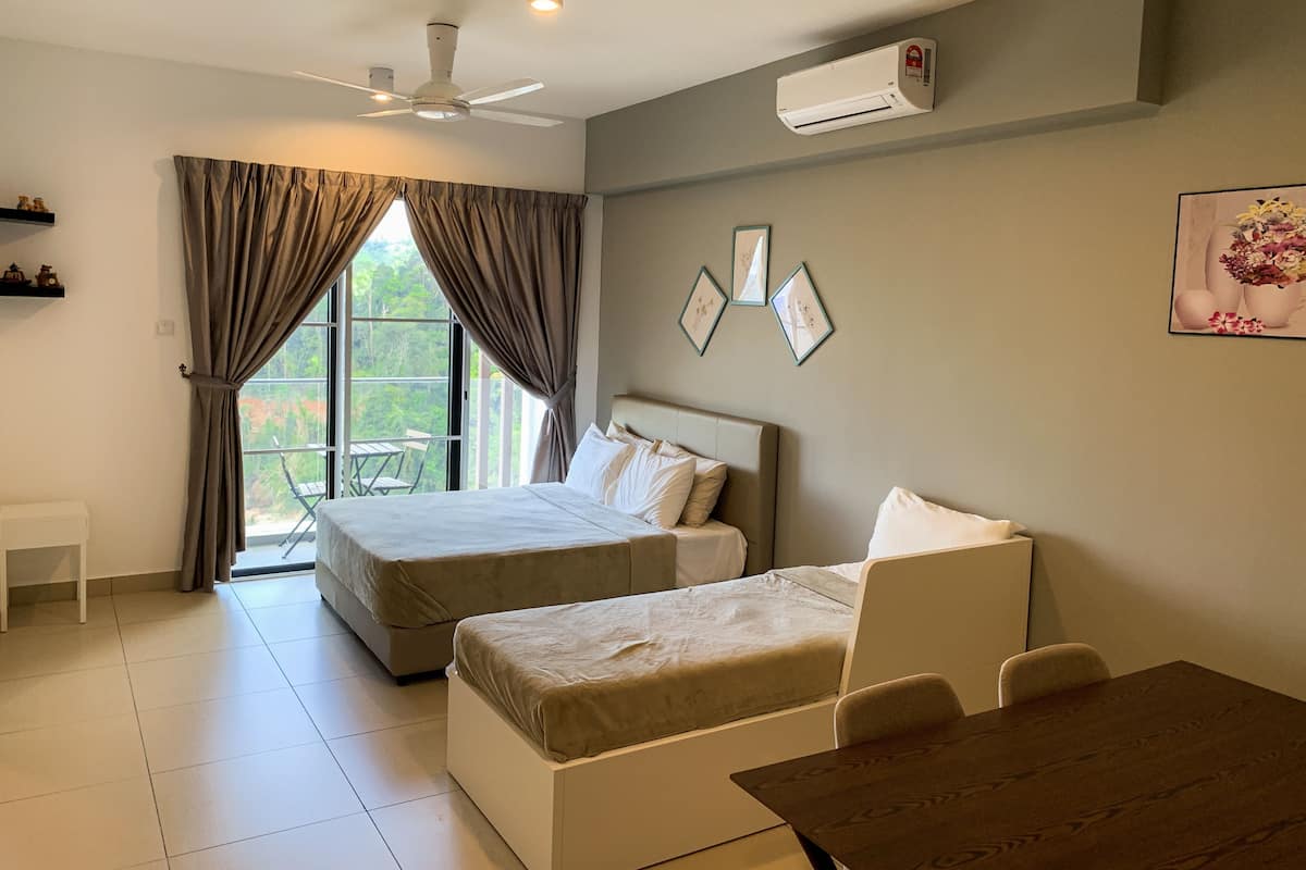 A hotel room with a bed, a sofa, a table, and an air conditioning unit.