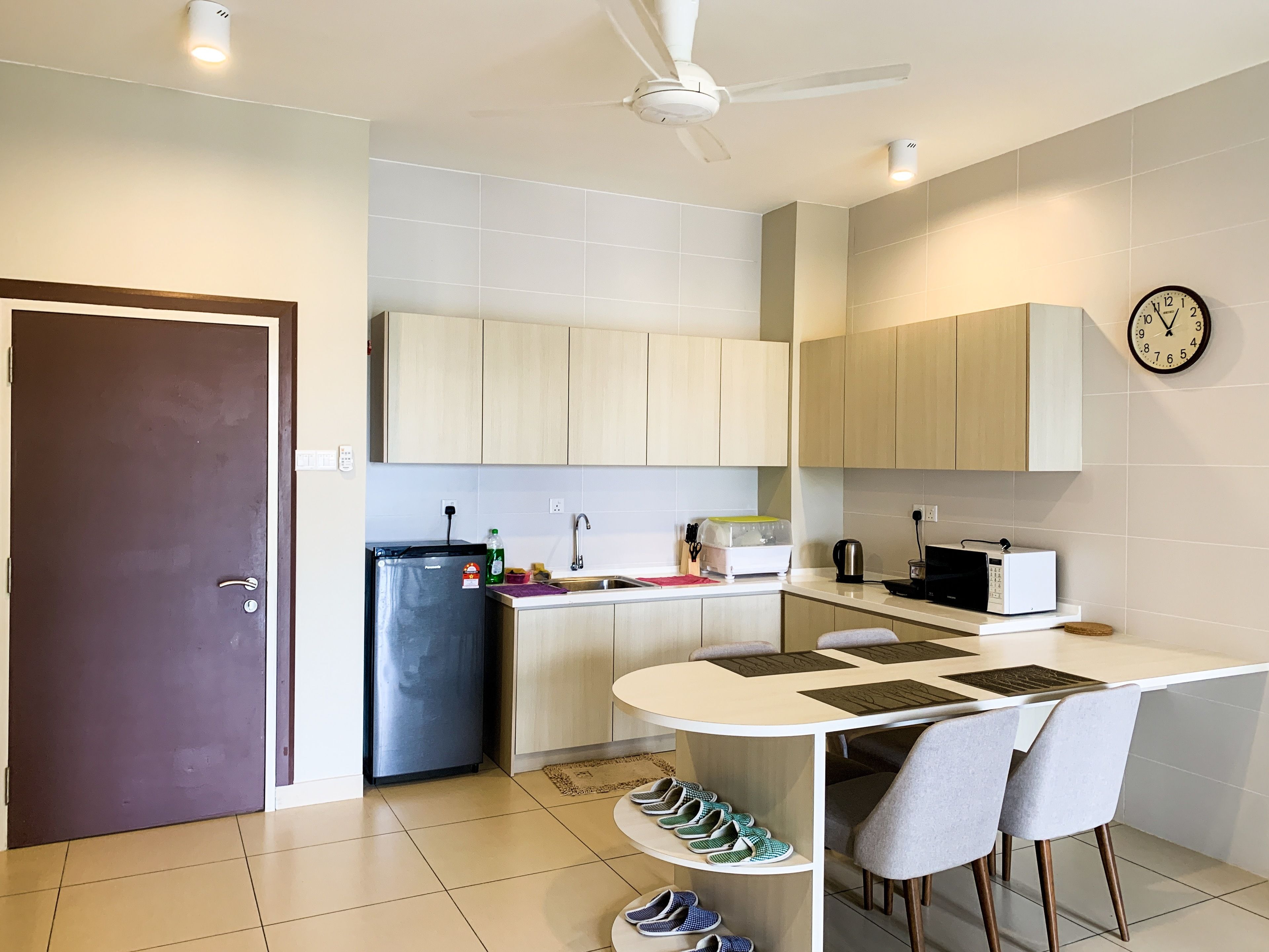 A modern kitchen with light wood cabinets, a refrigerator, a microwave, and a dining area with a table and chairs.