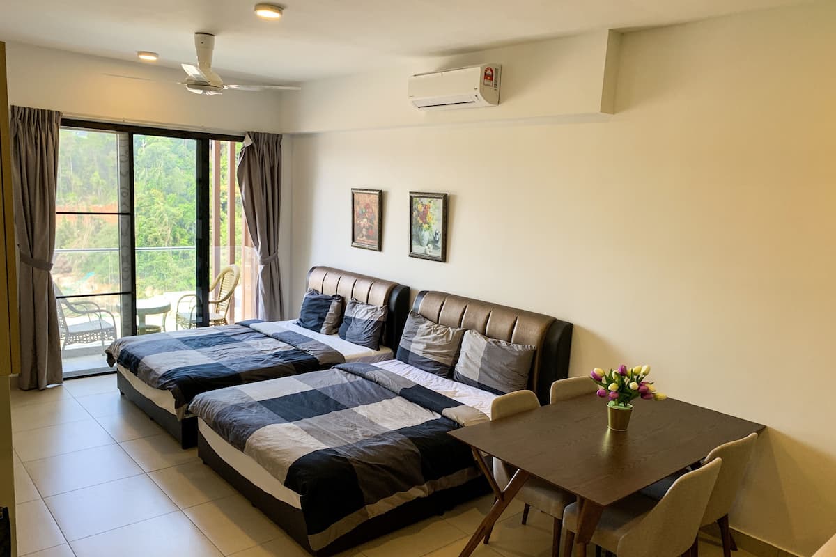 A hotel room with two beds, a dining table, and chairs. There is a balcony with a view of greenery.