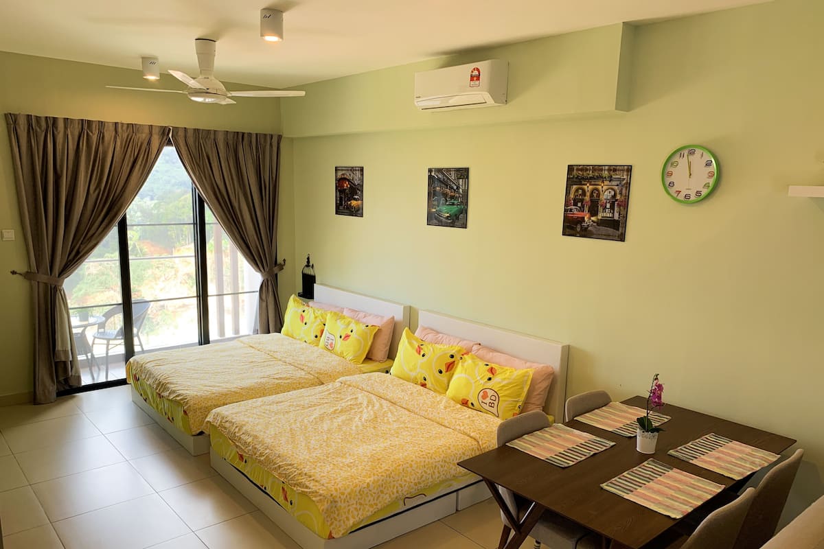 A hotel room with two beds, a dining table, and a view of greenery outside.