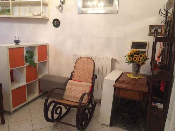 A cozy living room with a rocking chair, a bookshelf, a radiator, and a vase with sunflowers.