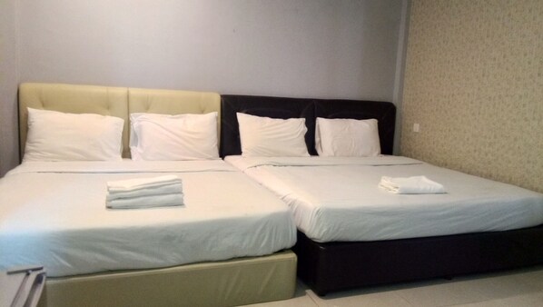 Two beds with white linens and towels, set against a neutral backdrop.