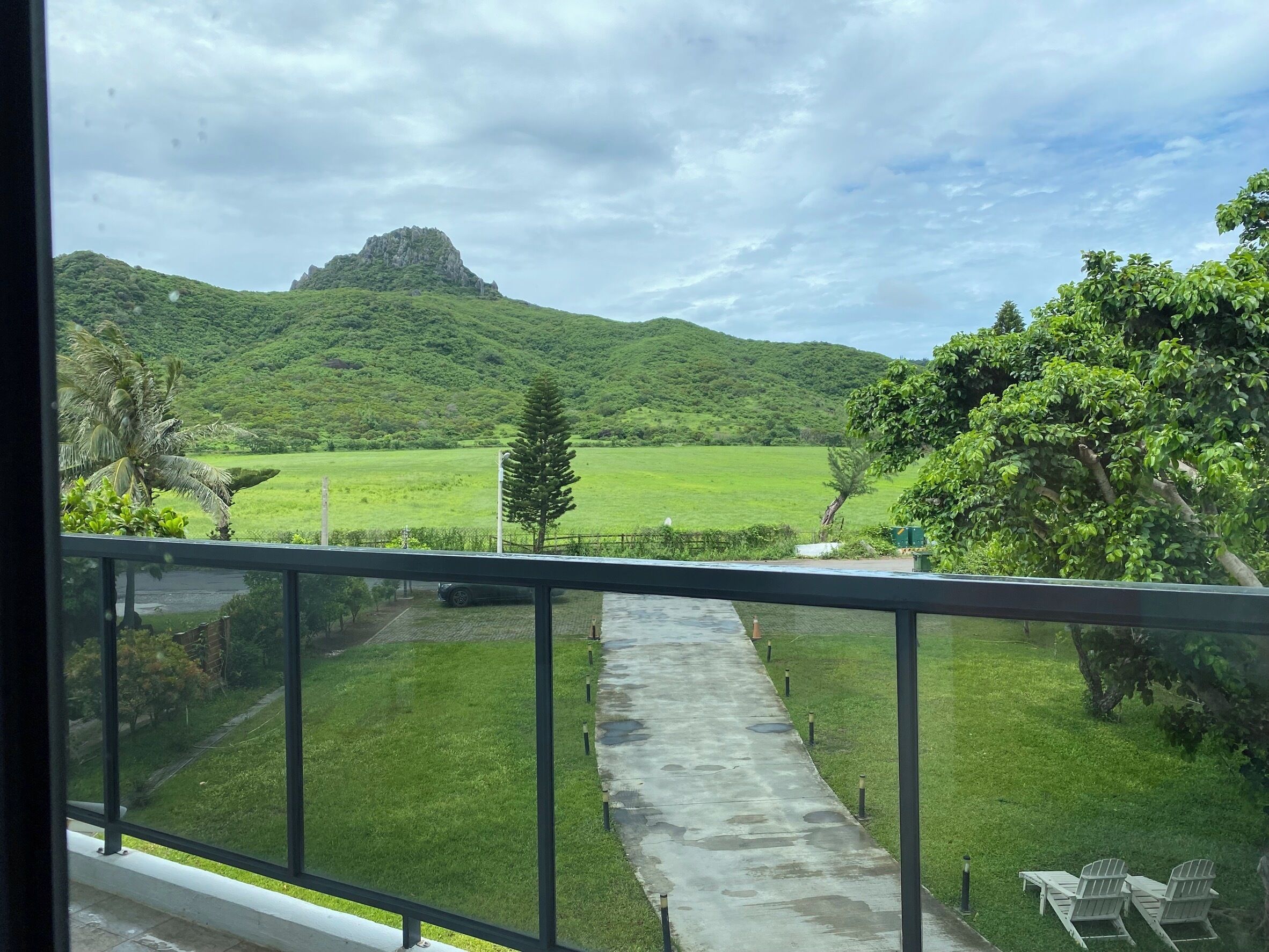 A balcony with a view of a green field, a mountain, and a clear sky.