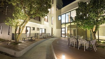 An outdoor patio area with wooden flooring, white chairs, and a table.