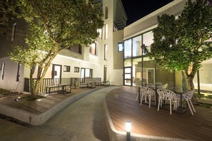 Un patio al aire libre con suelo de madera, sillas blancas y una mesa.