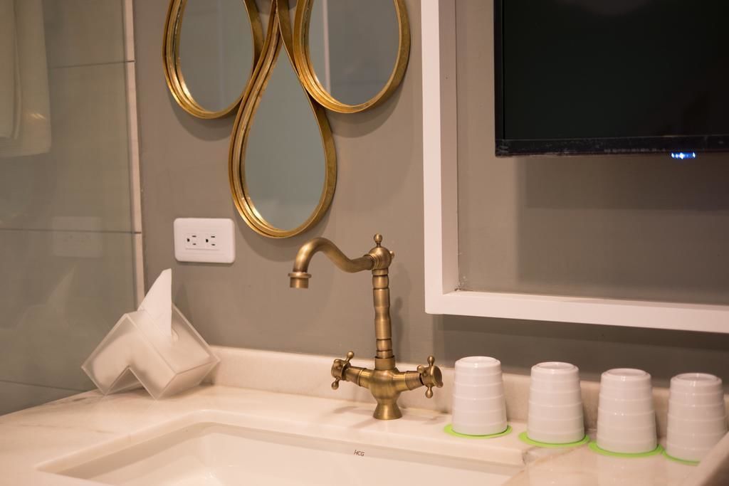 Un baño con lavamanos, un grifo dorado, un espejo y un televisor colocado sobre el espejo.