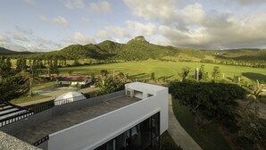 Un edificio moderno con tetto piano e ampie finestre, affacciato su un paesaggio verdeggiante con una collina che si staglia all'orizzonte.